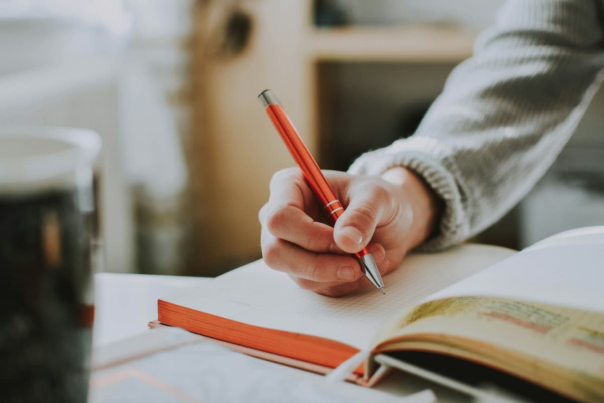 Person holding a red pen while writing or reviewing notes in a book